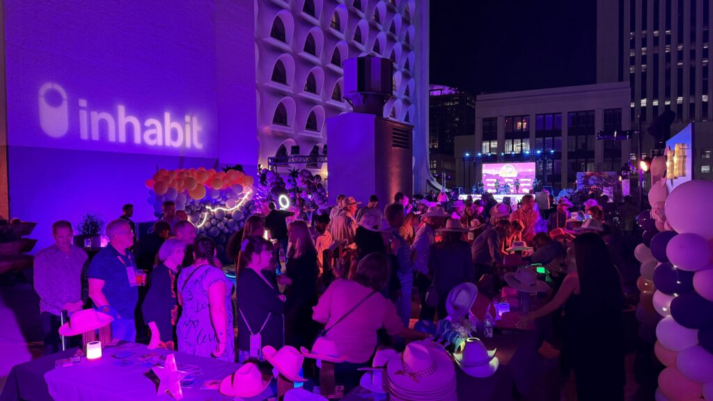 Guests at the Lasso the Stars rooftop party, with a cowboy hat bar and an Inhabit logo projected on the wall